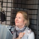Esther Wane smiling in her professional studio with microphone.