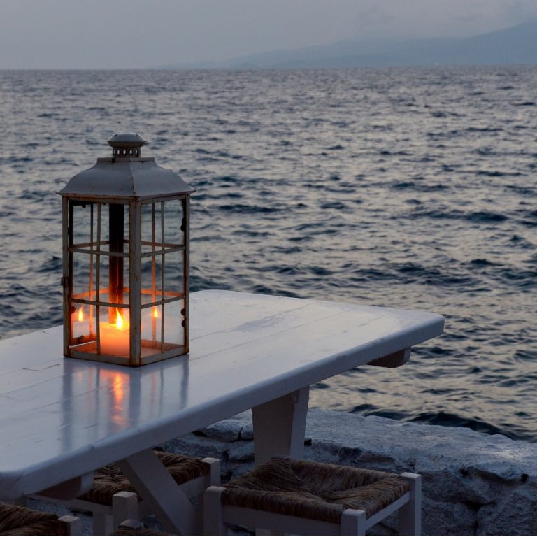 A lantern with a flickering candle on a table next to the ocean